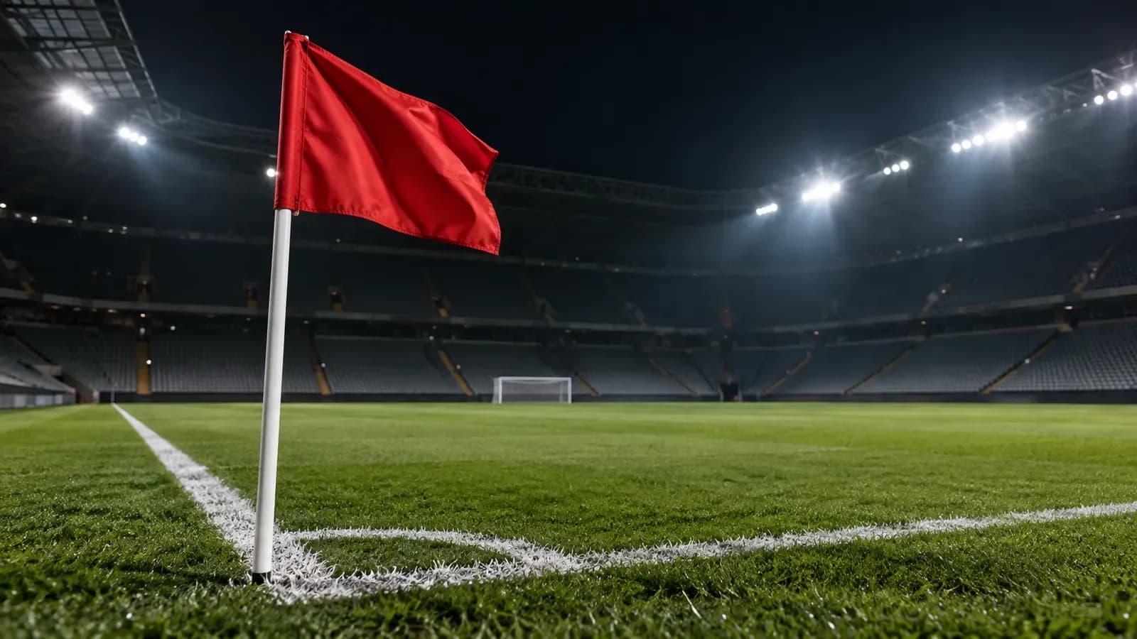 Foto generata con IA: Una bandierina del calcio d'angolo a tinta unita mossa dal vento all'incrocio delle linee bianche di un campo da gioco. Ripresa ravvicinata dal basso nella luce serale dei riflettori prima dell'incontro, con le gradinate deserte dello stadio che sfumano nella penombra dello sfondo. Nessuna persona, scritta, numero, marchio, stemma o sponsor è visibile nell'inquadratura.